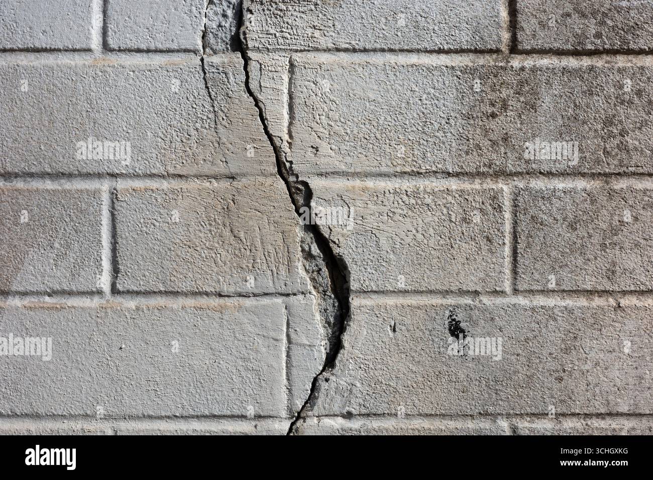 Gros plan d'un mur de briques grises altérées avec une fissure verticale proéminente traversant le centre. Banque D'Images