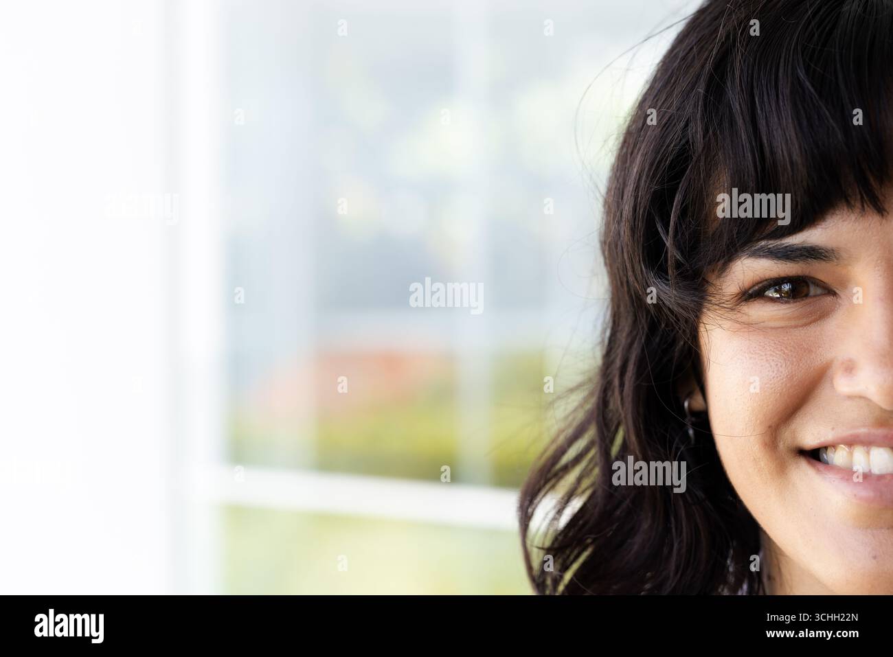 Femme souriante avec les cheveux foncés assis par la fenêtre, profitant de la journée ensoleillée, à la maison, espace de copie Banque D'Images