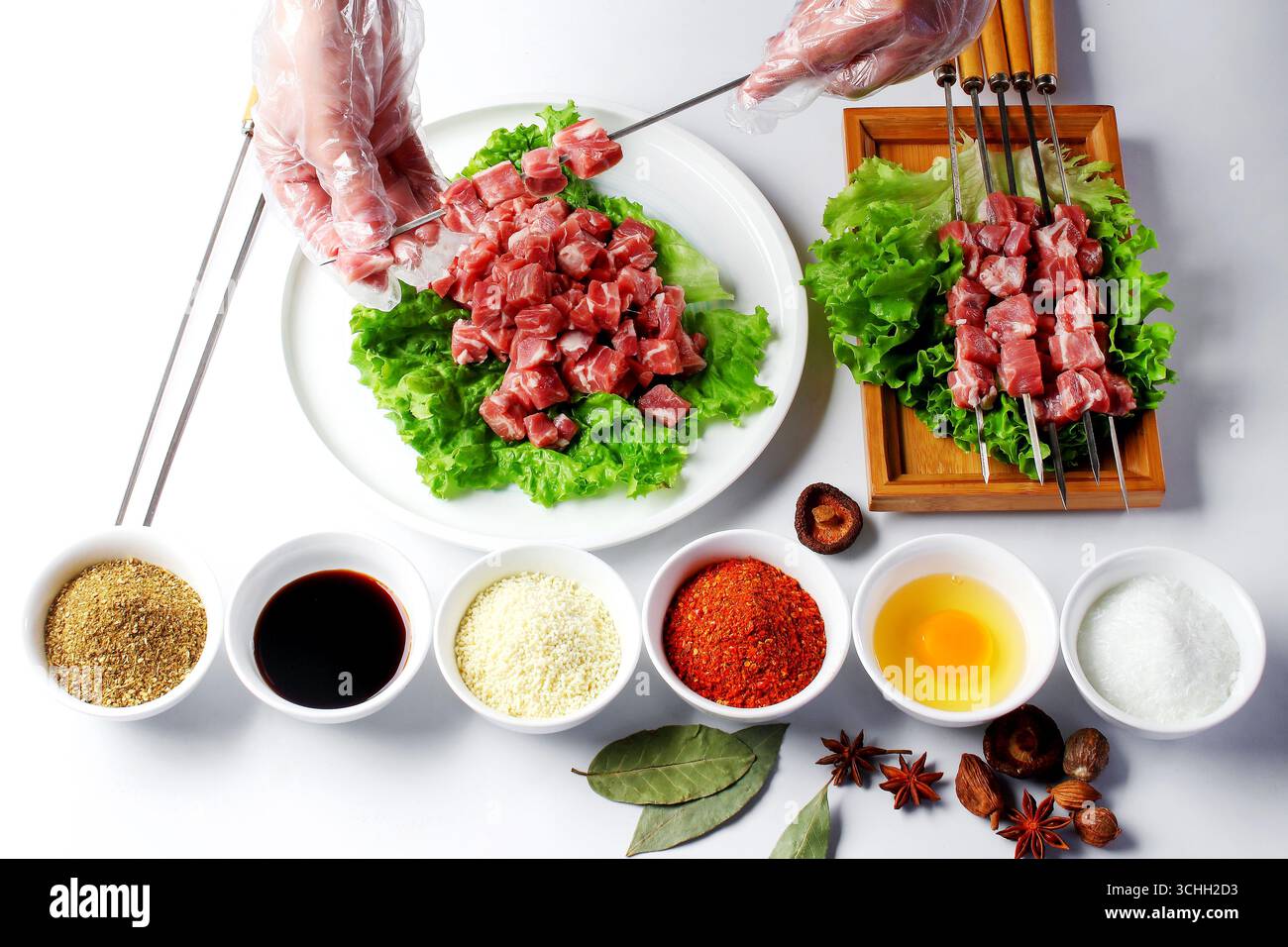 Mains gantées brochant l'agneau cru pour Kebabs avec des épices Banque D'Images