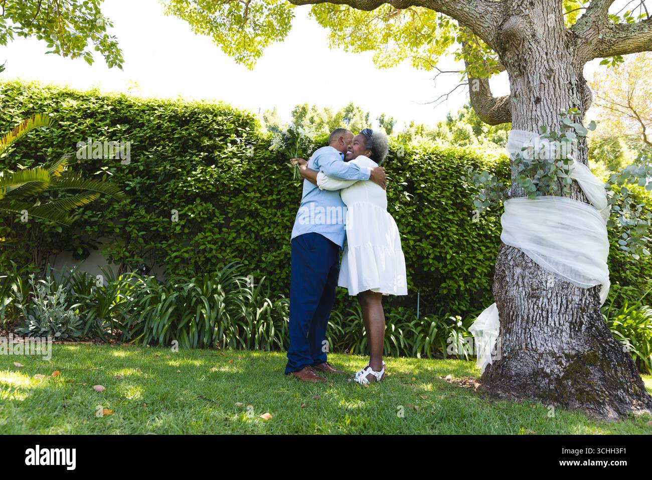 Au mariage, couple Senior embrassant sous l'arbre dans le jardin, profitant d'une journée ensoleillée ensemble Banque D'Images