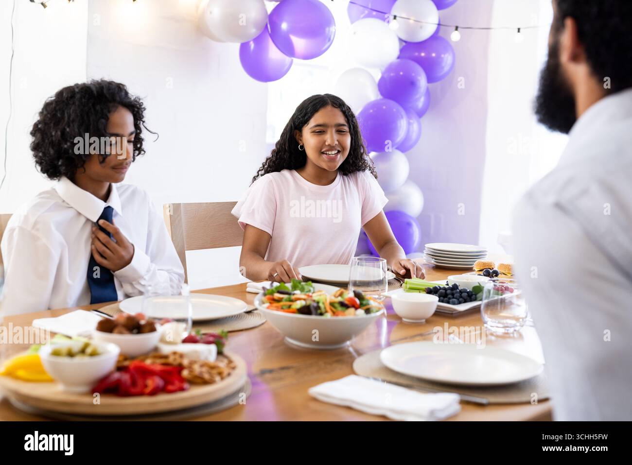 Famille diversifiée appréciant un repas de fête ensemble à table avec des décorations colorées, à la maison Banque D'Images