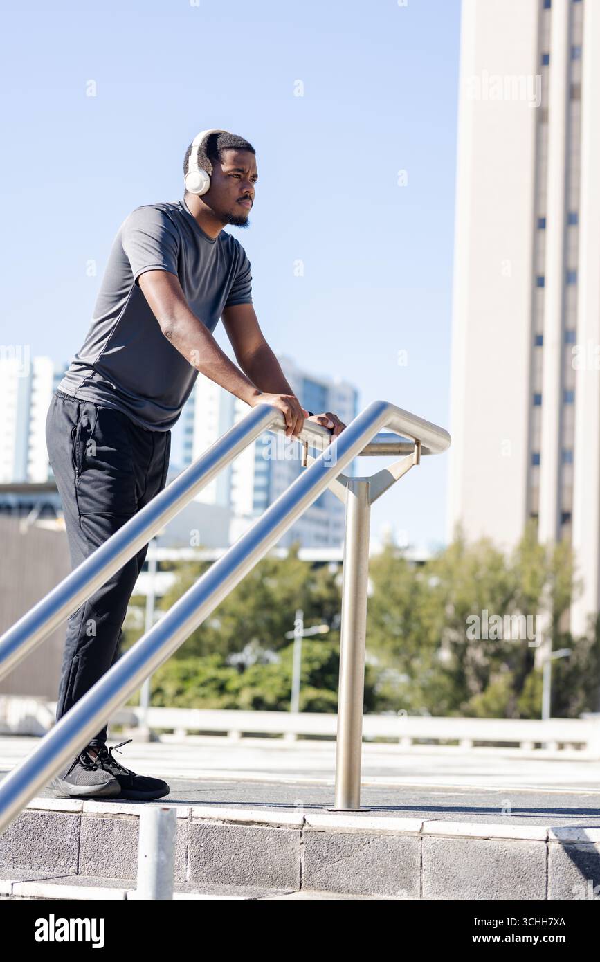 Homme afro-américain portant des vêtements de sport et des écouteurs appuyés sur la main courante sur la terrasse Banque D'Images