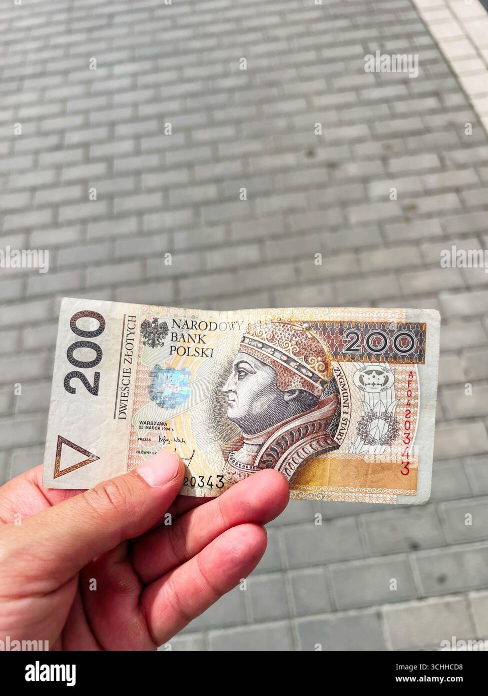 Rzeszow, Pologne - 22 août 2025 : gros plan d'une main tenant un billet de banque polonais de 200 zloty contre des carreaux pavés Banque D'Images