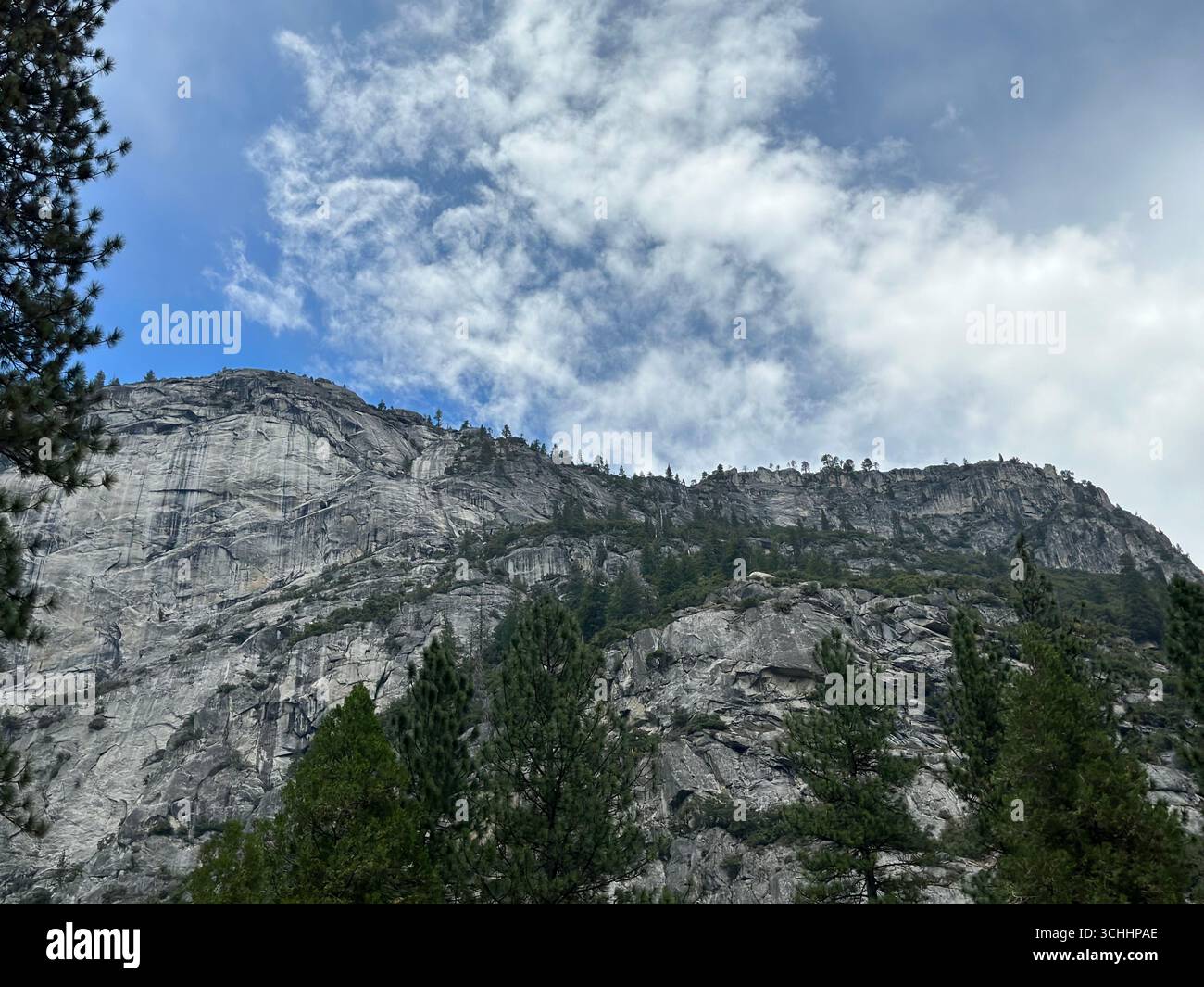 Majestueuses falaises de granit s'élevant au-dessus des pins dans le parc national de Yosemite, en Californie, sous un ciel bleu partiellement nuageux. - Image de stock capturée avec un smartphone