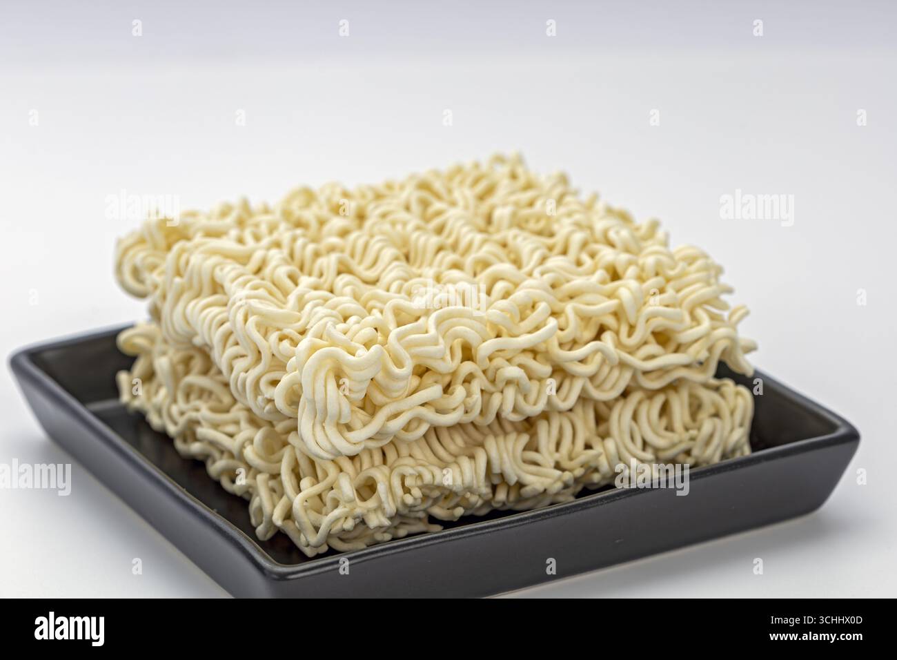 Un bloc de nouilles instantanées non cuites sur la plaque noire RAW ramen carré sec pâtes ondulées beige couleur simple nourriture minimale style studio léger fond propre co Banque D'Images