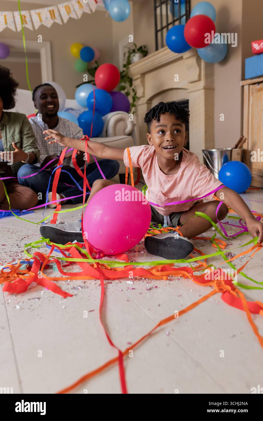 Enfant jouant avec des banderoles colorées et des ballons à la maison, célébrant joyeusement Banque D'Images