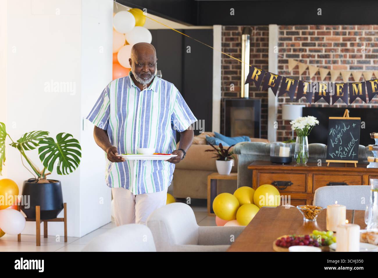 Homme portant plateau avec de la nourriture à la fête de retraite, entouré de décorations festives Banque D'Images