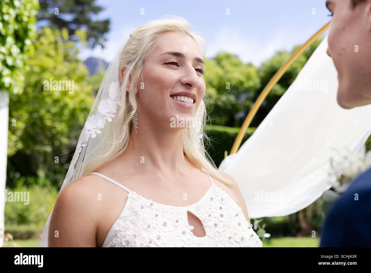 Mariée souriant joyeusement lors de la cérémonie de mariage en plein air, entourée de verdure luxuriante Banque D'Images