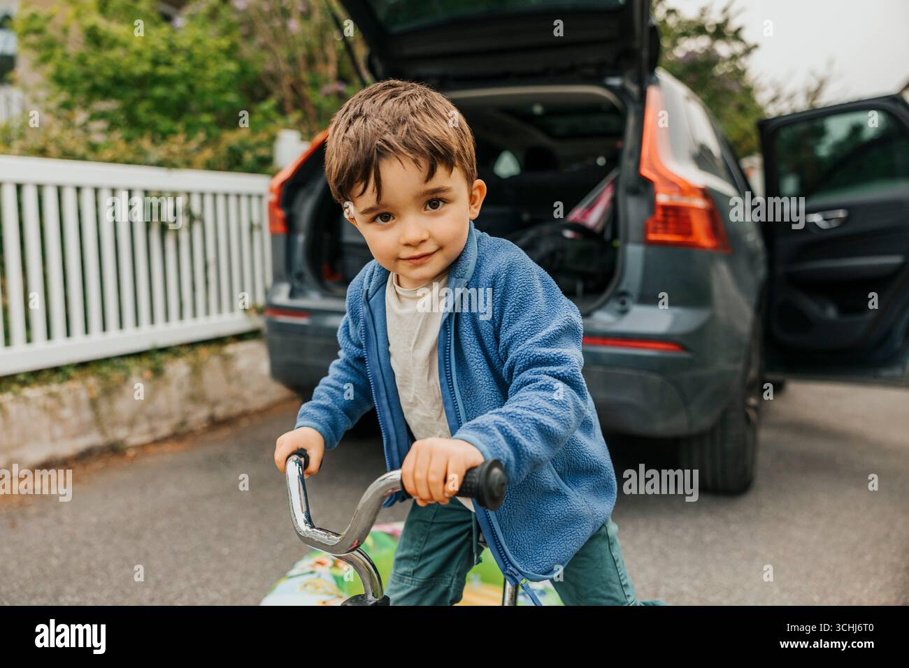 Portrait de vélo d'équilibre de garçon mignon en face de la voiture Banque D'Images