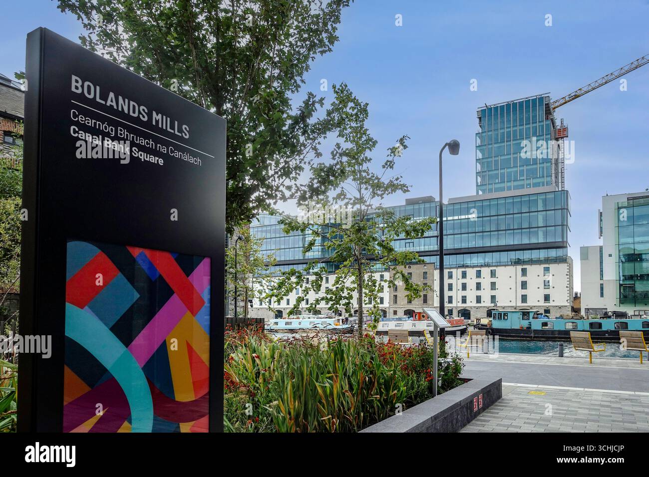 Panneau pour Bolands Mills canal Bank Square, Dublin Docklands, Irlande, avec des bureaux en verre modernes, des entrepôts historiques et des bateaux amarrés sur le canal en vue. Banque D'Images