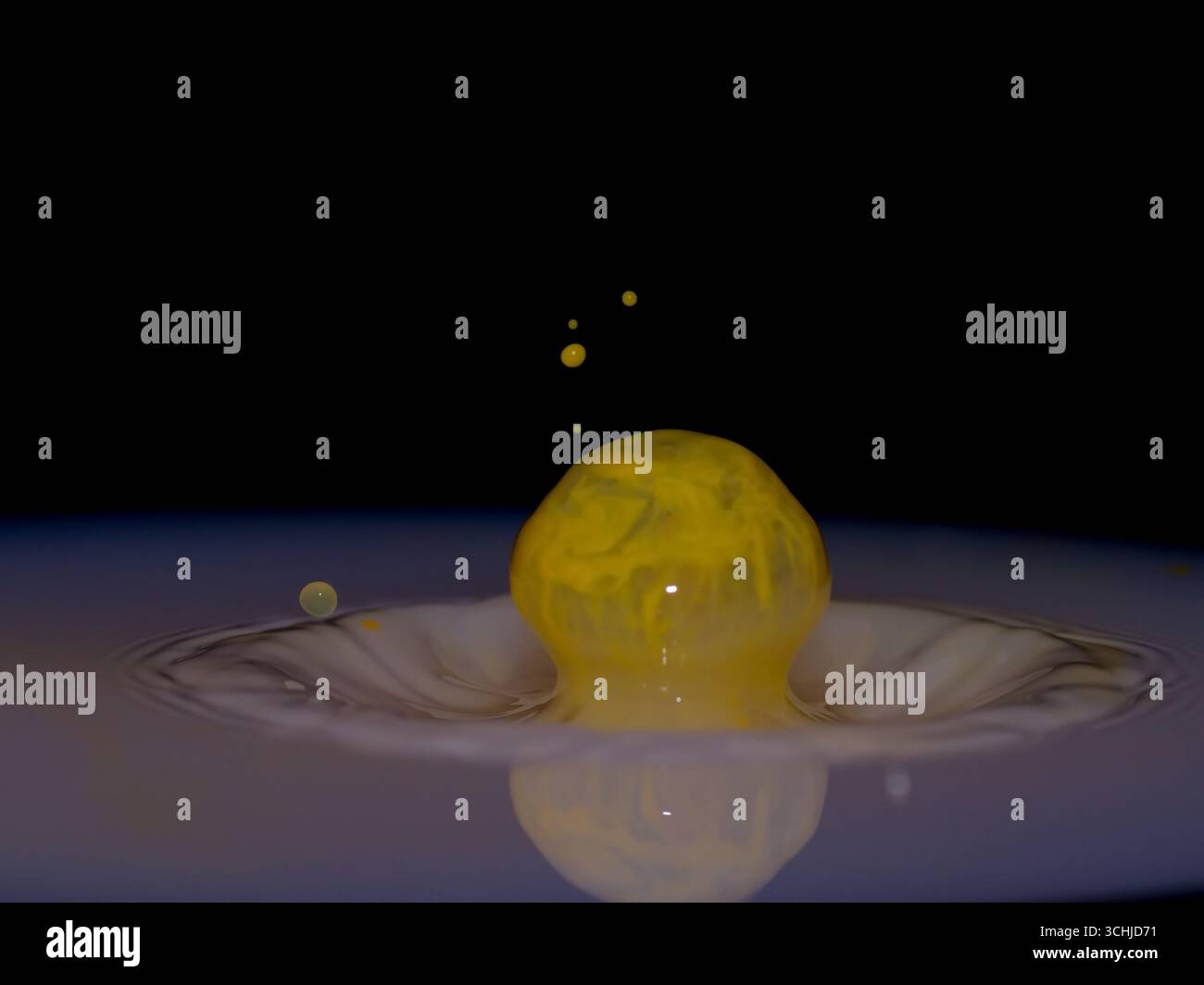 La gouttelette liquide jaune rebondit d'une piscine, formant un dôme lisse et des perles secondaires sur un fond noir, capturé avec macro haute vitesse. Banque D'Images