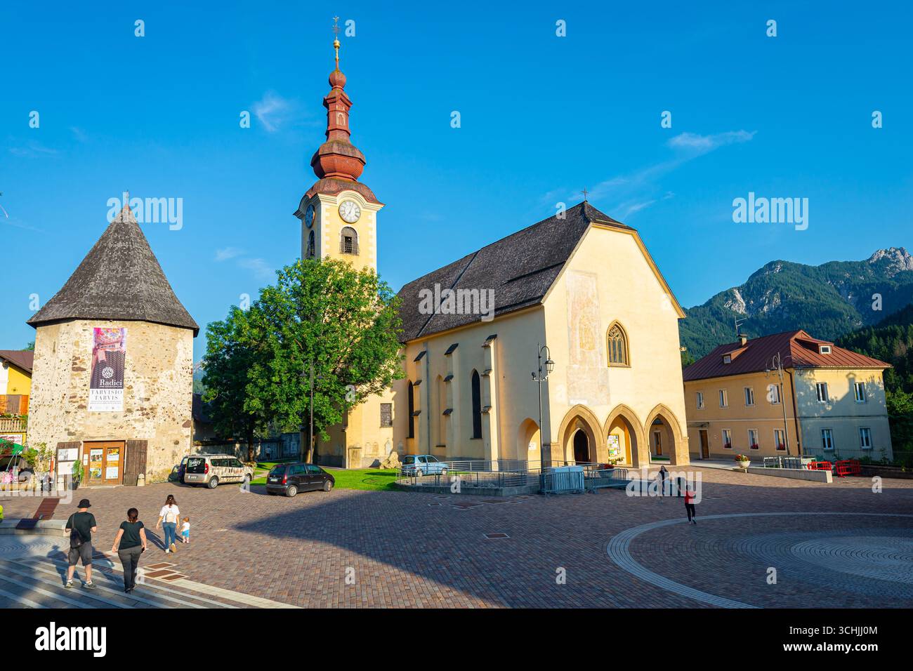 Charmante place du village avec église historique et tour au coucher du soleil à Tarvisio, Italie Banque D'Images
