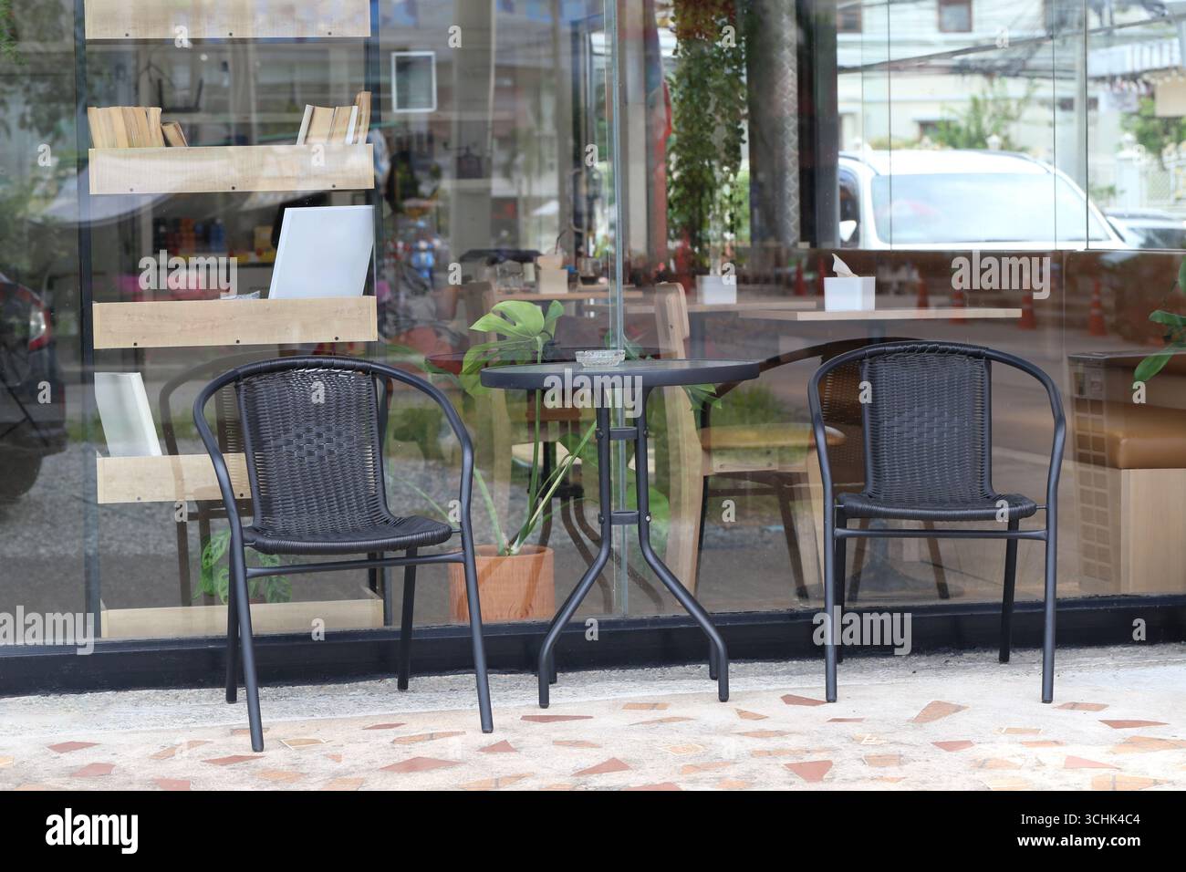 Un charmant coin salon extérieur avec deux chaises noires et une table ronde à côté d'une vitrine, ornée de plantes, créant un accueil et rela Banque D'Images