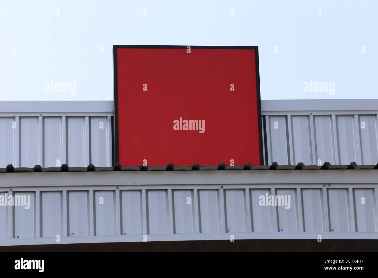 Un panneau rouge vif monté sur un bâtiment moderne se distingue sur un ciel bleu clair, offrant un élément de design minimaliste parfait pour divers nous Banque D'Images