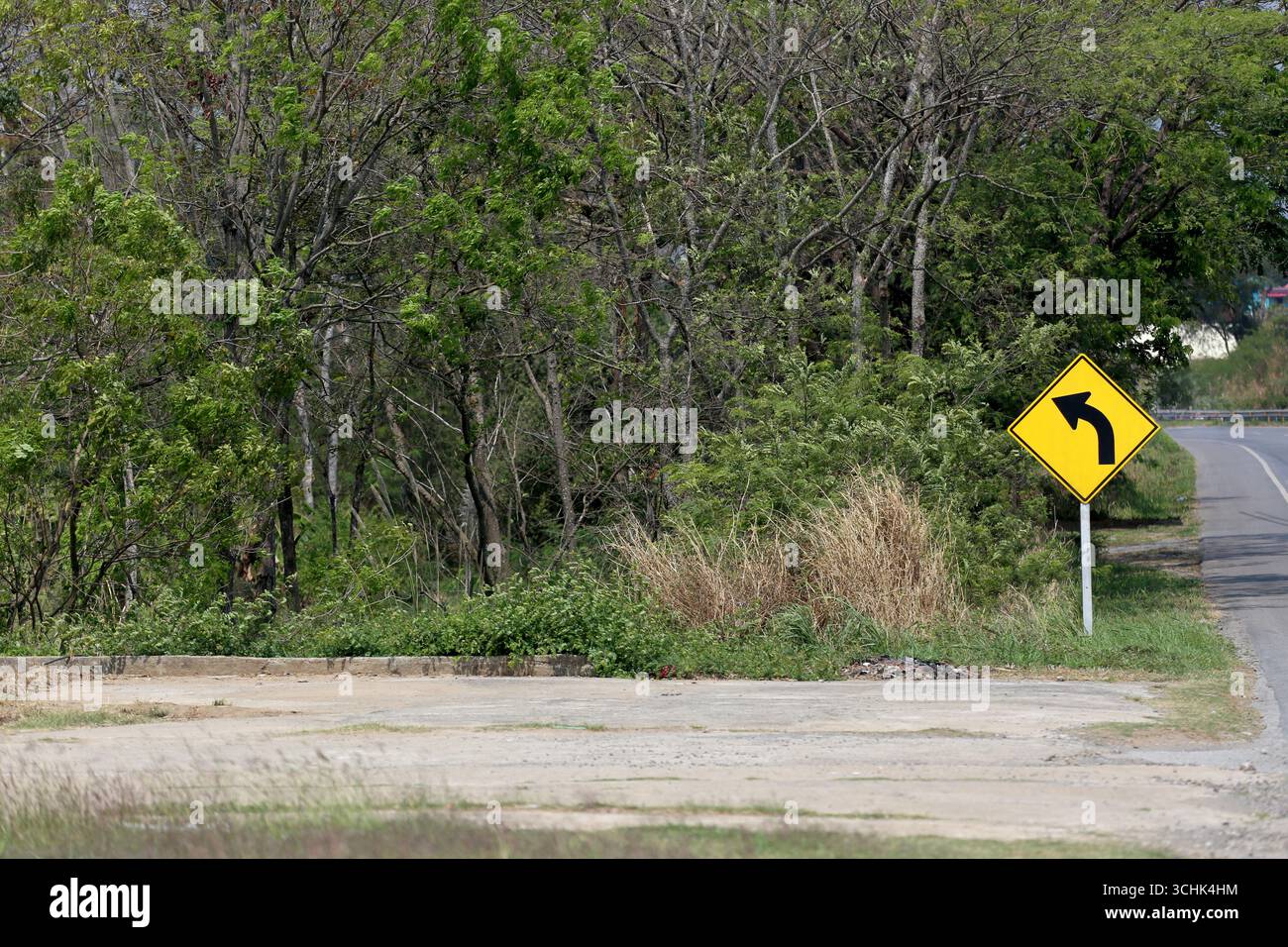 Un panneau routier jaune vif indique un virage à droite, entouré de verdure luxuriante et d'arbres. La scène capture l'essence du voyage rural et sûr Banque D'Images