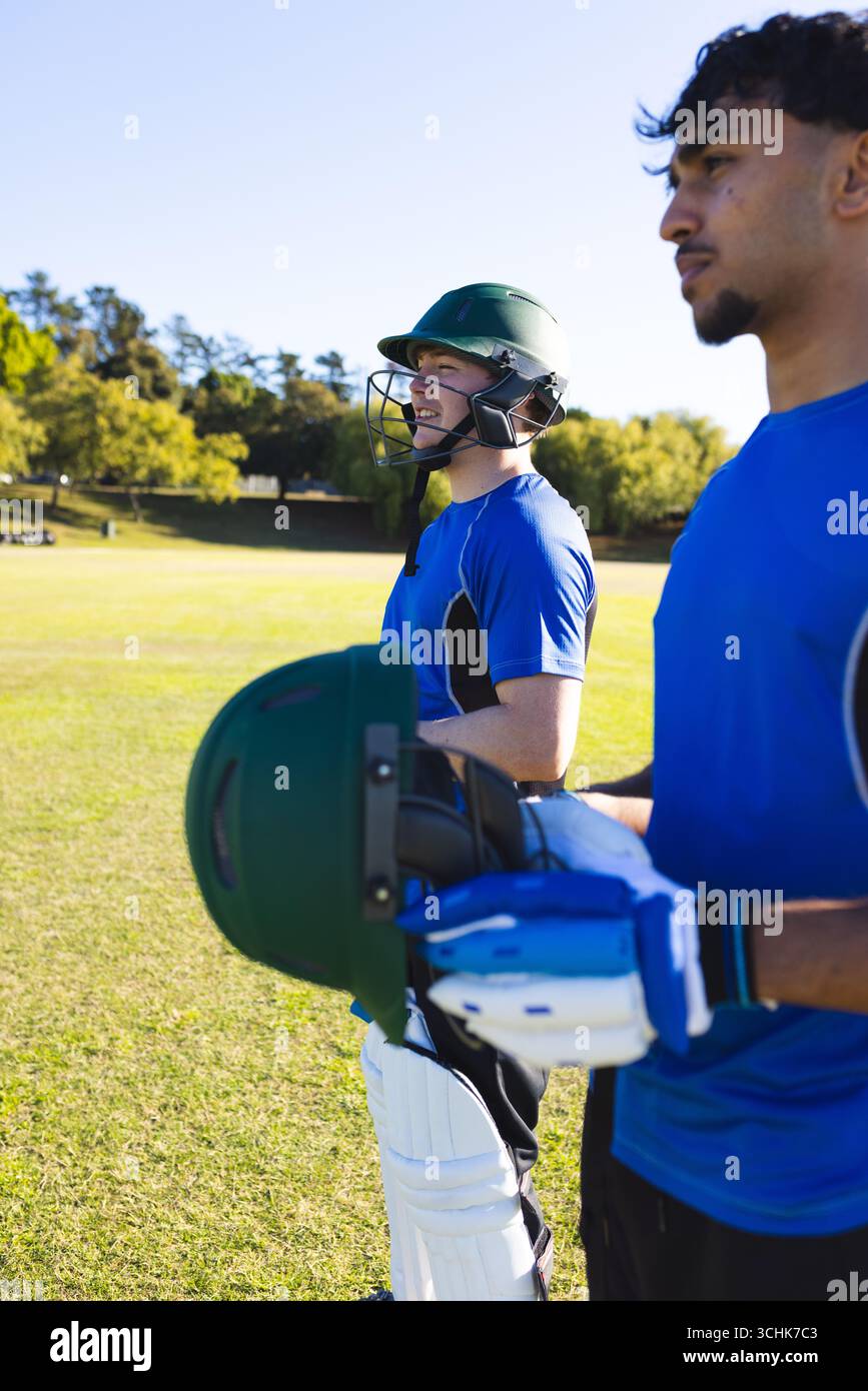 Divers coéquipiers masculins en maillots bleus debout sur le terrain de cricket avec des casques et des gants de frappe Banque D'Images