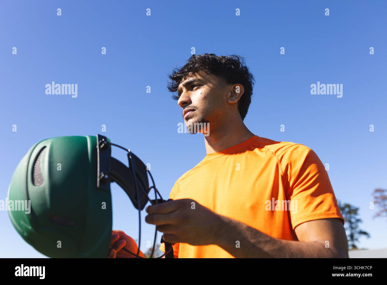 Homme indien debout au parc sous ciel bleu clair avec casque de sport vert par des sangles Banque D'Images