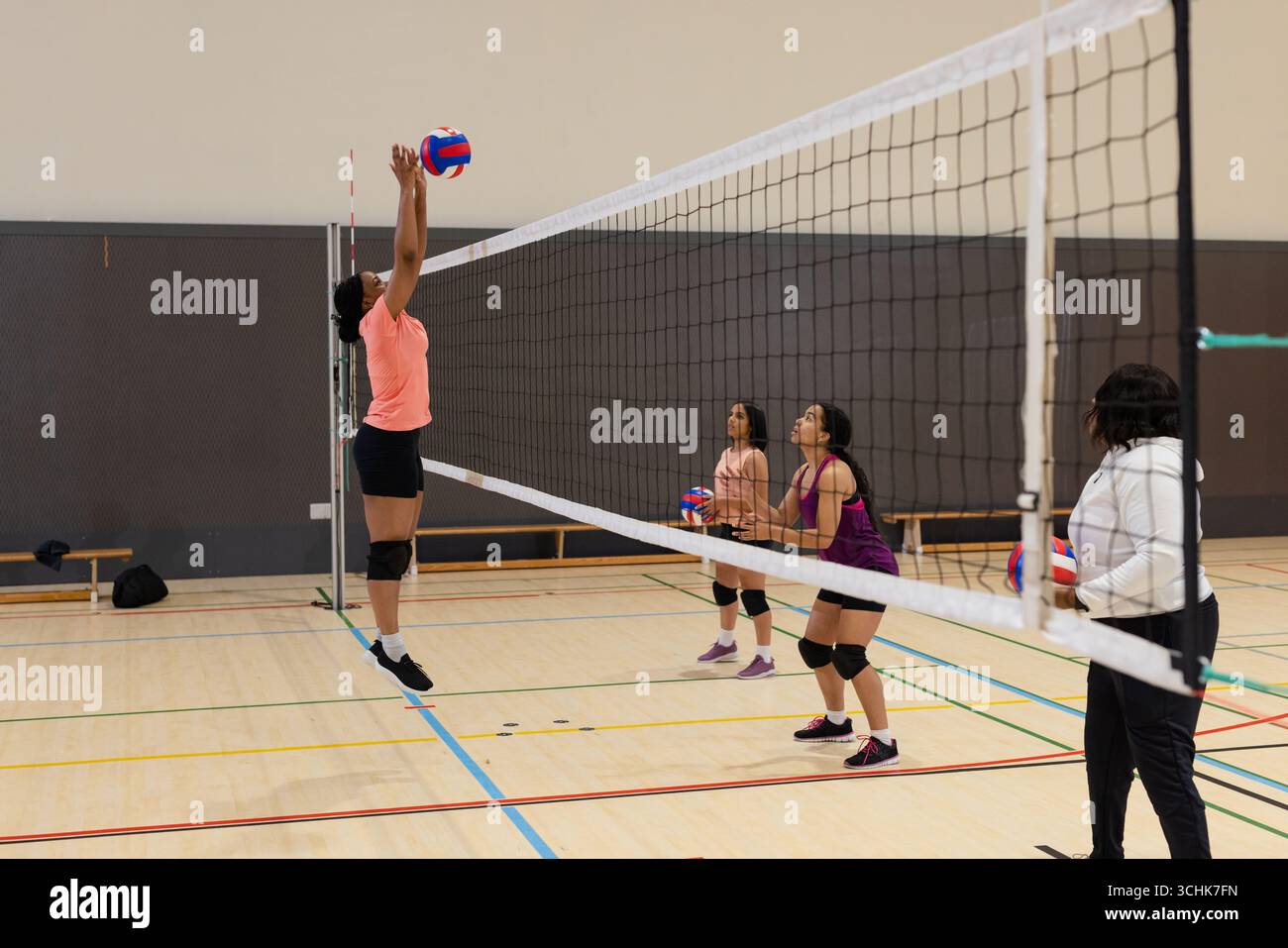 Diverses coéquipières féminines pratiquant le volley-ball au filet sur le terrain dans la salle de gym, volley-ball, espace copie Banque D'Images