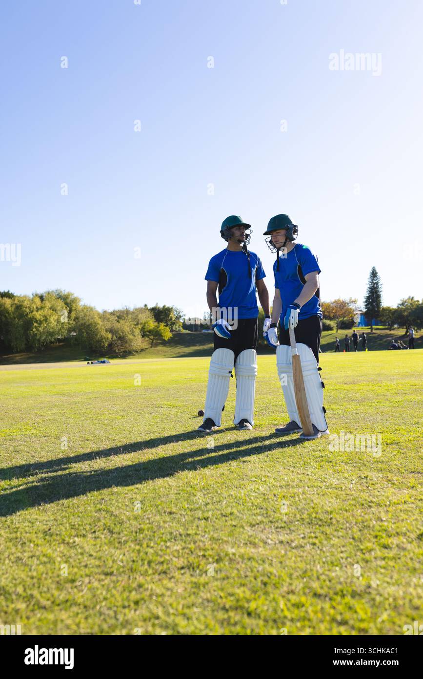 Divers coéquipiers masculins debout sur un terrain ensoleillé avec des battes de cricket dans un équipement de protection Banque D'Images