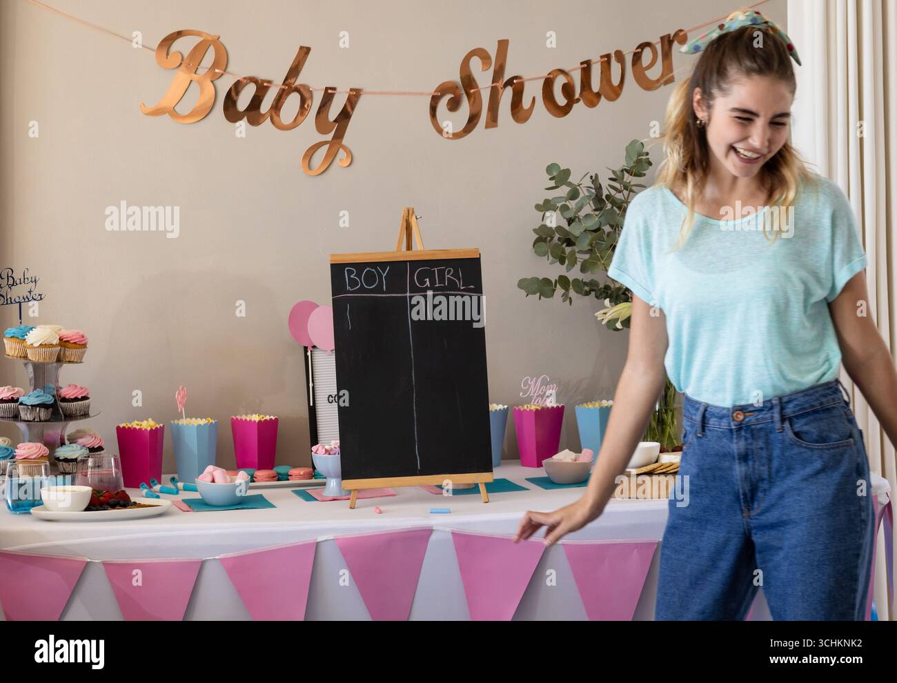 Femme souriante profitant de la fête de douche de bébé avec table décorée et cupcakes, à la maison Banque D'Images