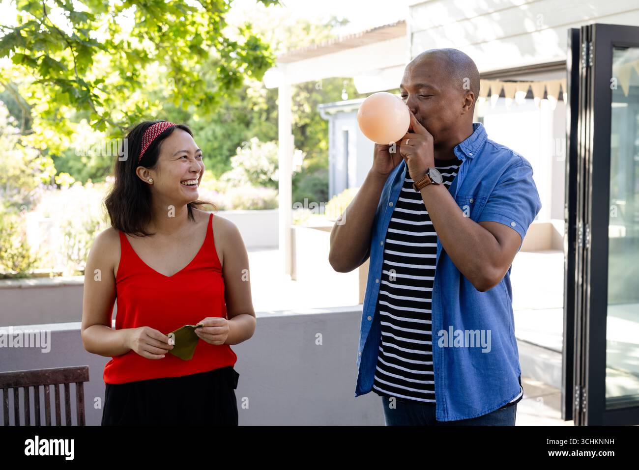 À la fête, homme afro-américain soufflant ballon tandis que femme en haut rouge souriant sur le pont Banque D'Images