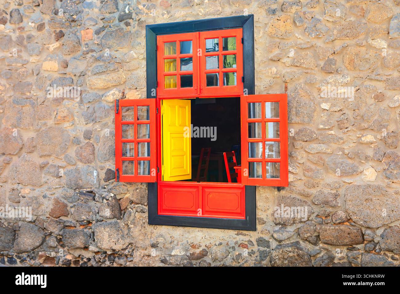 Fenêtre peinte créative et mur de pierre. Fenêtre orange vif avec cadres de volets ouverts contre un mur de pierre rugueux. À travers la fenêtre, un lumineux Banque D'Images