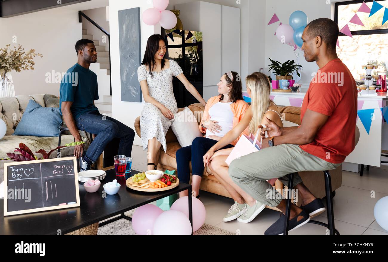 Divers amis appréciant la fête de douche de bébé avec des collations et des décorations dans le salon, à la maison Banque D'Images