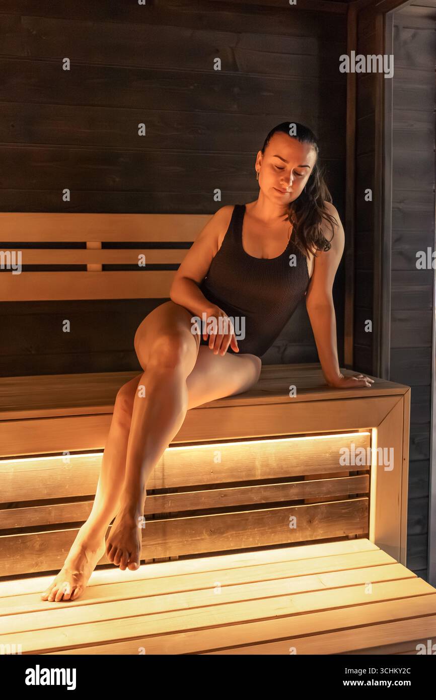 Femme sur le banc de sauna, lumière ambre chaude. Moment de détente. Banque D'Images