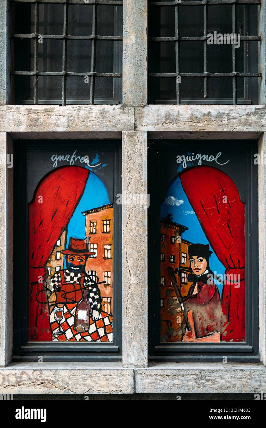 Art de fenêtre coloré peint représentant les personnages traditionnels lyonnais de marionnettes Guignol et Gnafron encadrés par des rideaux rouges dans le Vieux Lyon, France Banque D'Images