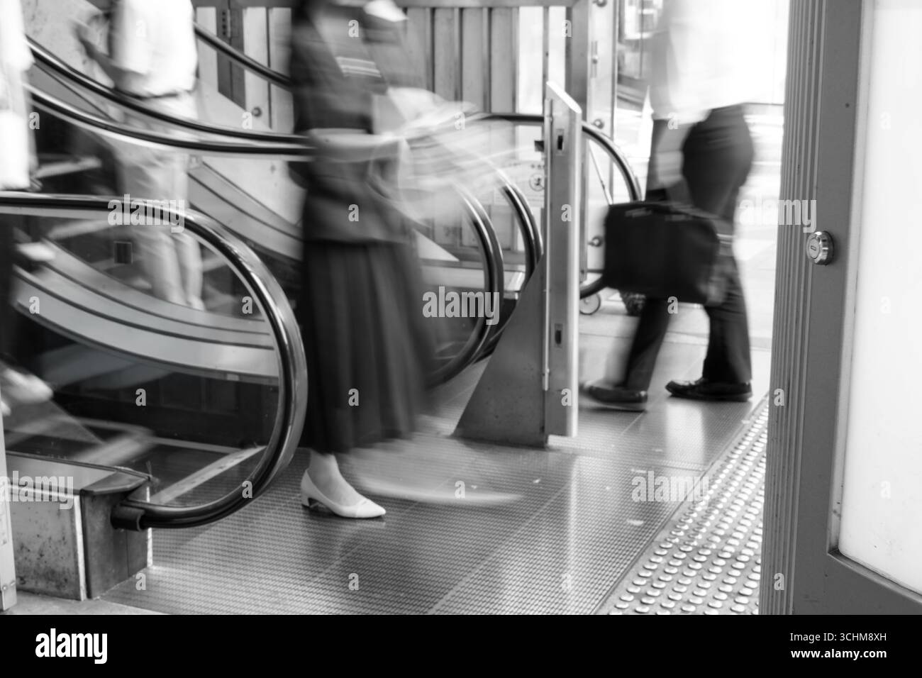 Femme d'affaires floue et homme avec escalator de sortie de mallette dans une scène monochrome capturant le mouvement, la vie moderne de la ville, et des moments fugaces Banque D'Images