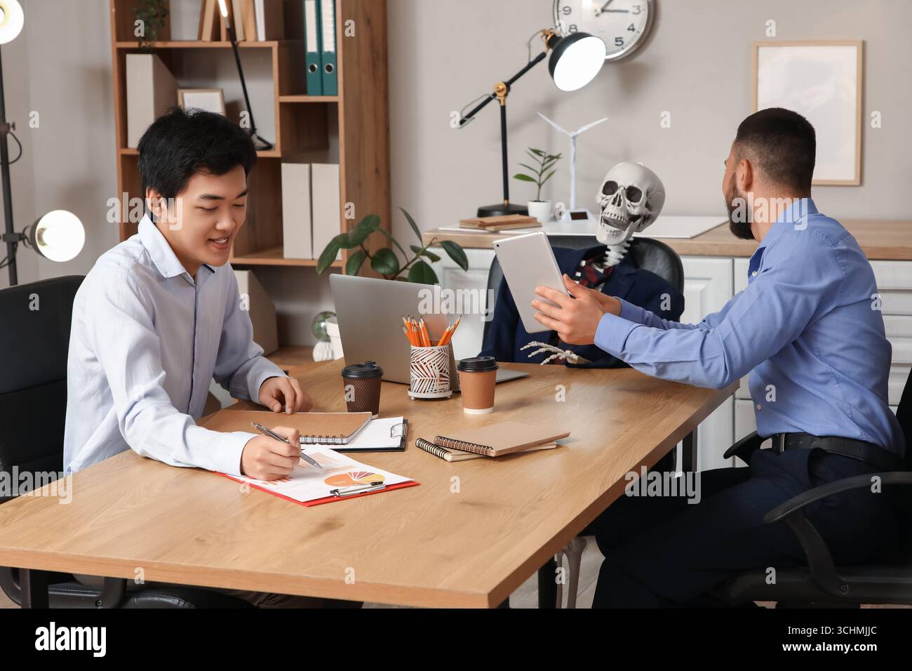 Collègues masculins avec squelette humain travaillant à table dans le bureau Banque D'Images