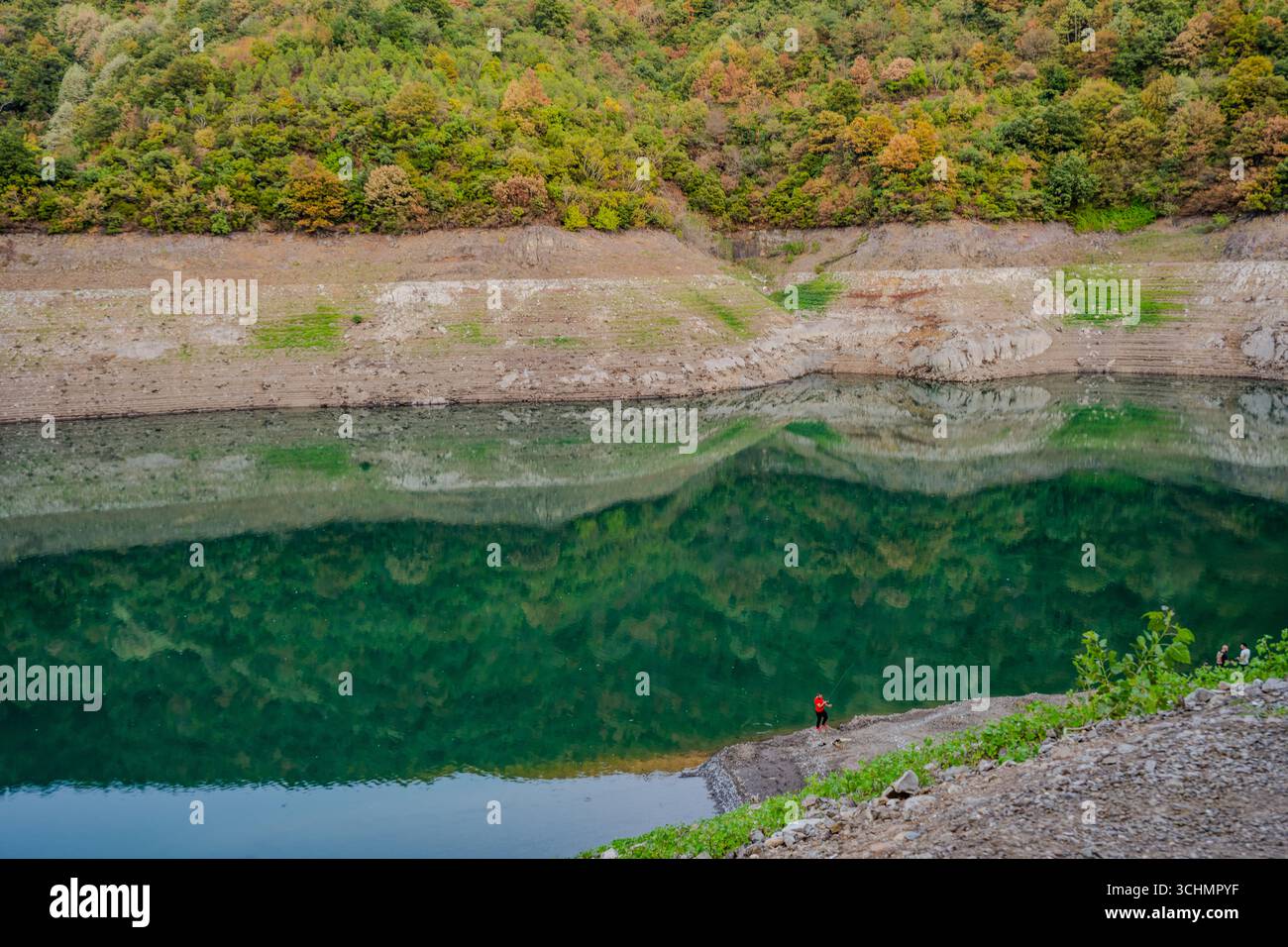 Une personne se tient au bord du lac du barrage de Yuvacık, où les collines boisées se reflètent dans l'eau verte calme à Yuvacık Yakacık, Başiskele, Kocaeli, T. Banque D'Images