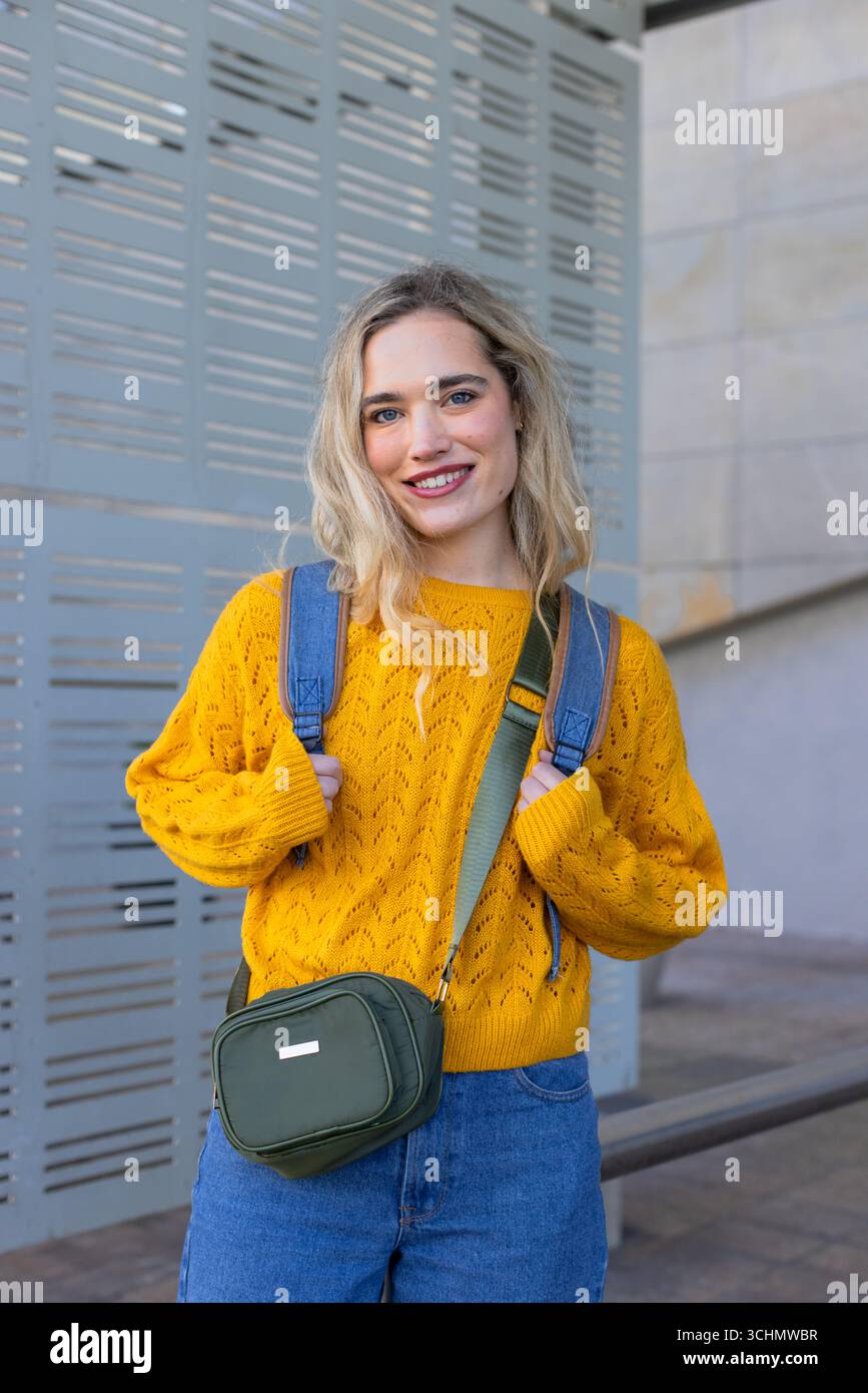 Femme debout tenant des sangles de sac à dos en pull jaune sur la passerelle pavée par panneau perforé Banque D'Images
