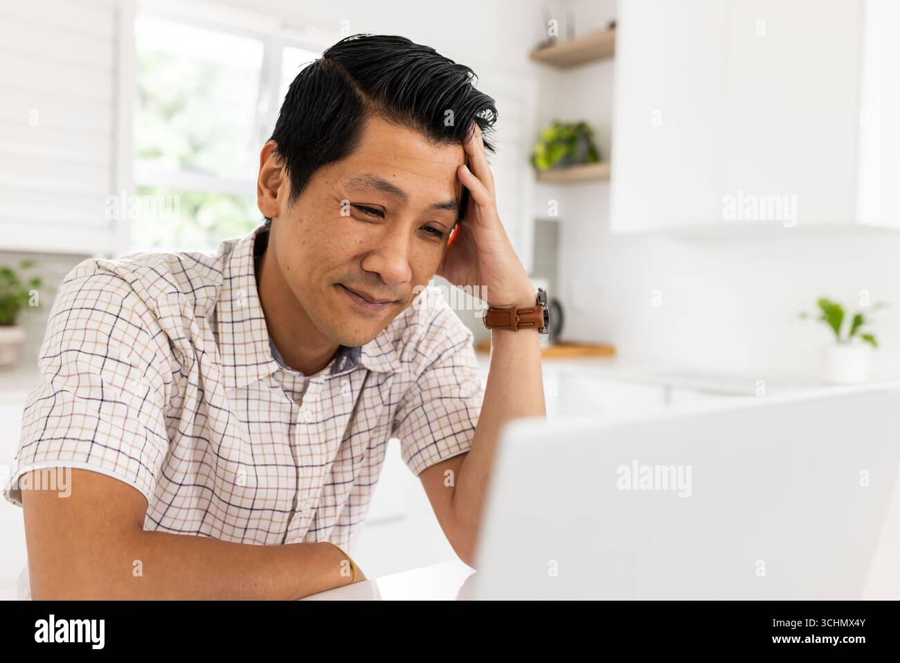 Homme asiatique souriant tout en utilisant un ordinateur portable à la maison, appréciant le contenu en ligne Banque D'Images