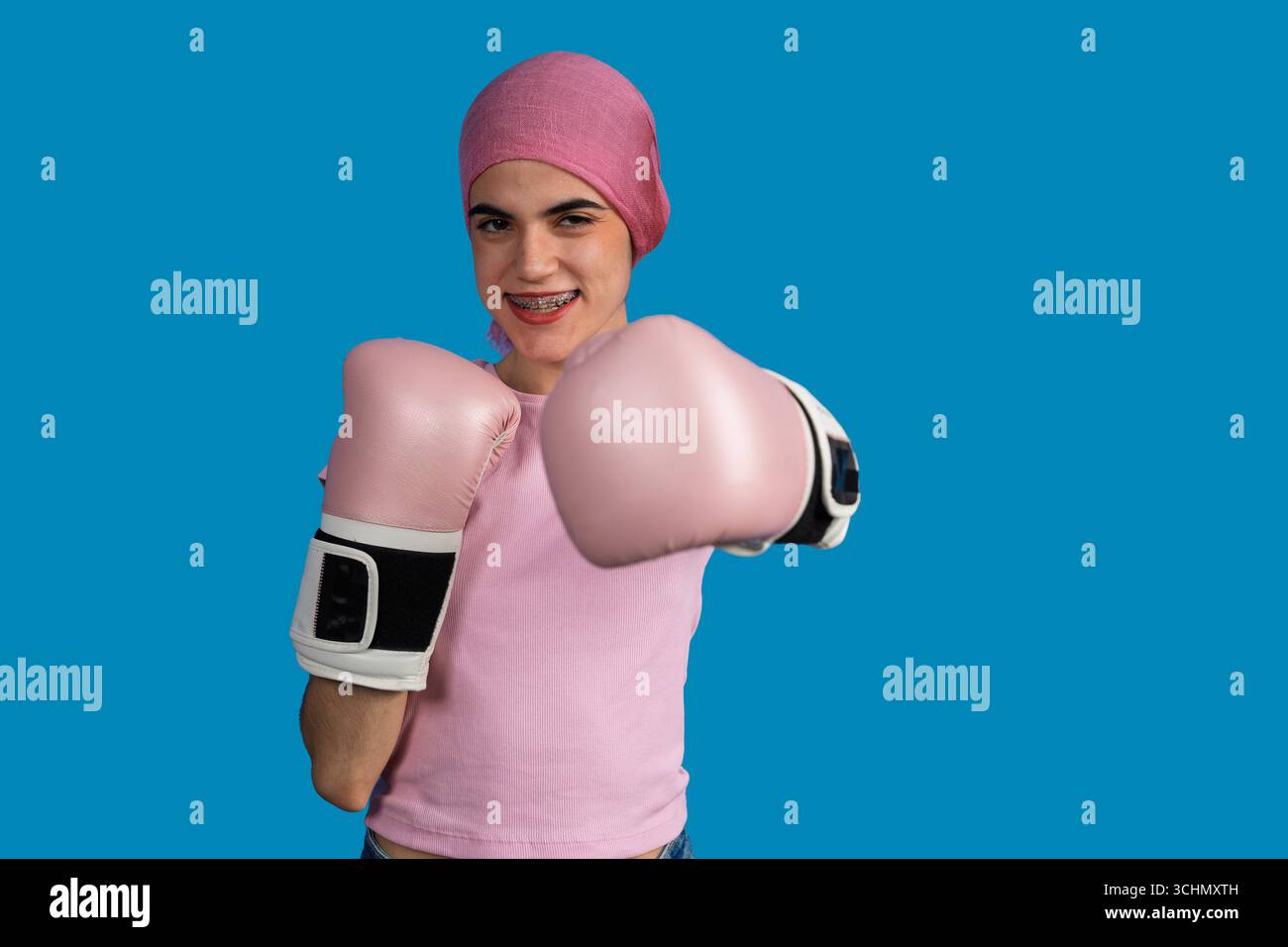 Jeune femme portant un foulard et des gants de boxe luttant contre le cancer avec une attitude positive Banque D'Images