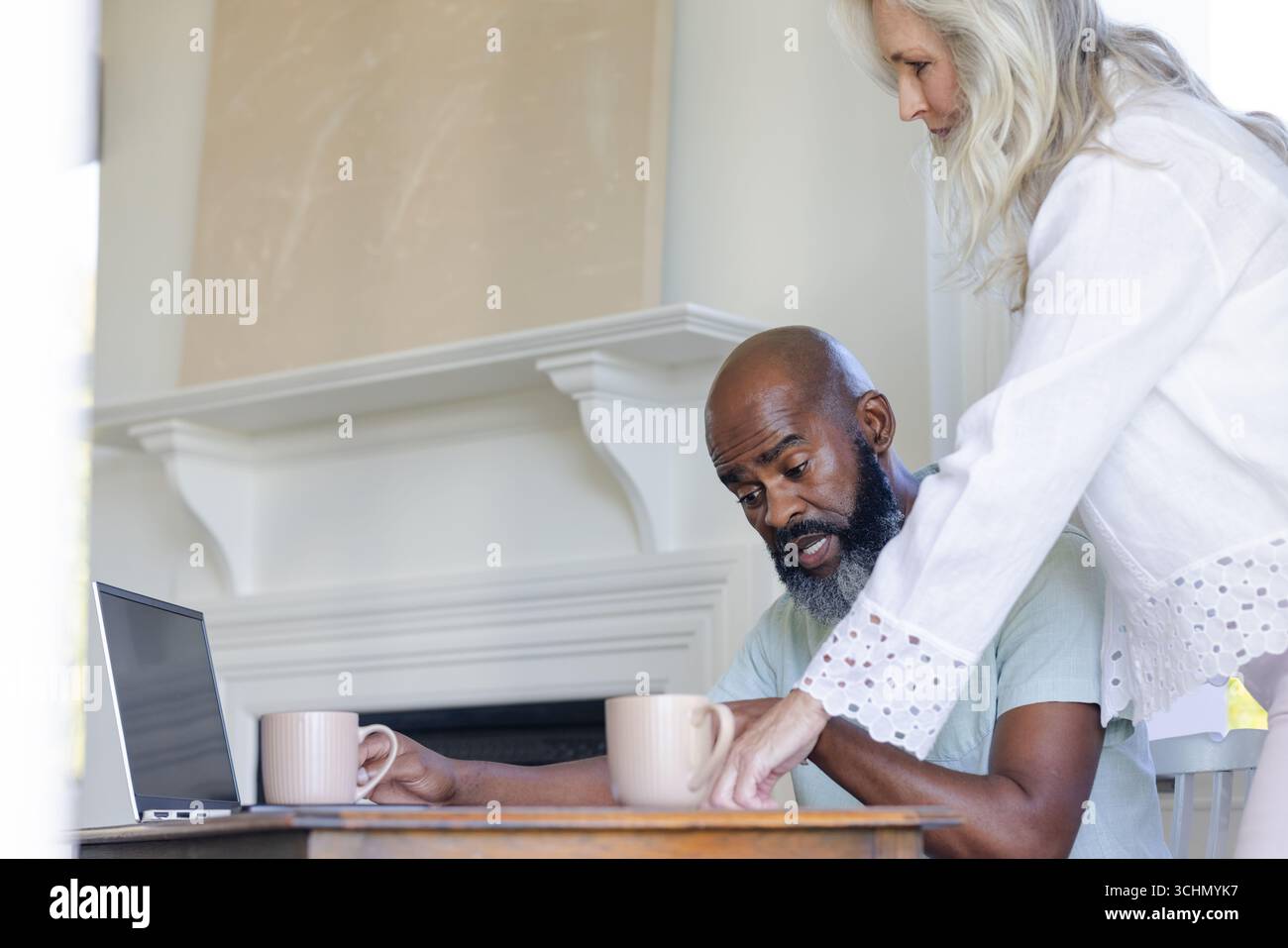 Couple mûr appréciant le café ensemble à la maison, en utilisant un ordinateur portable sur la table Banque D'Images