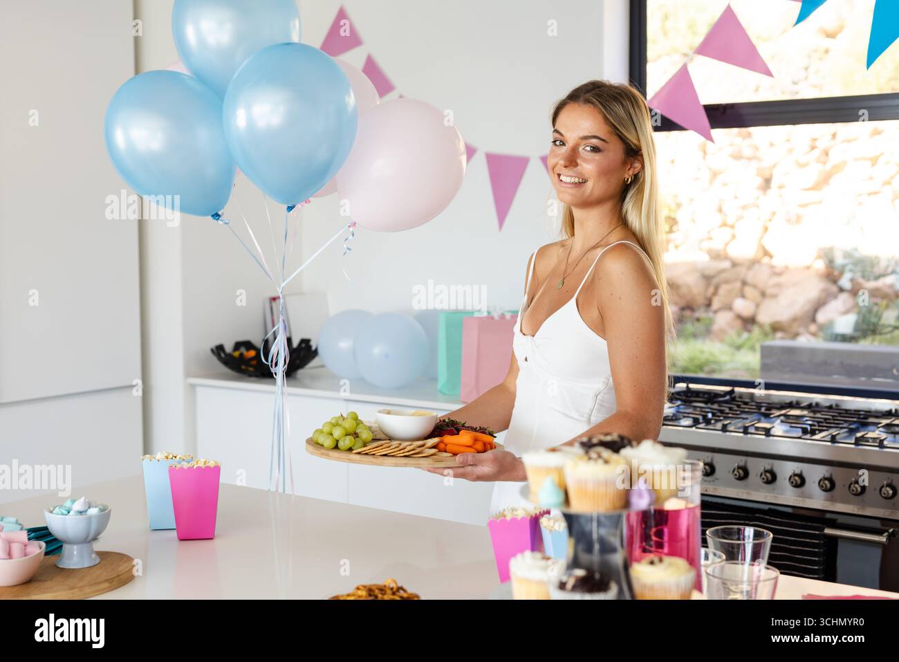 Douche de bébé, femme souriante tenant un plateau avec des collations à la fête d'anniversaire dans la cuisine Banque D'Images