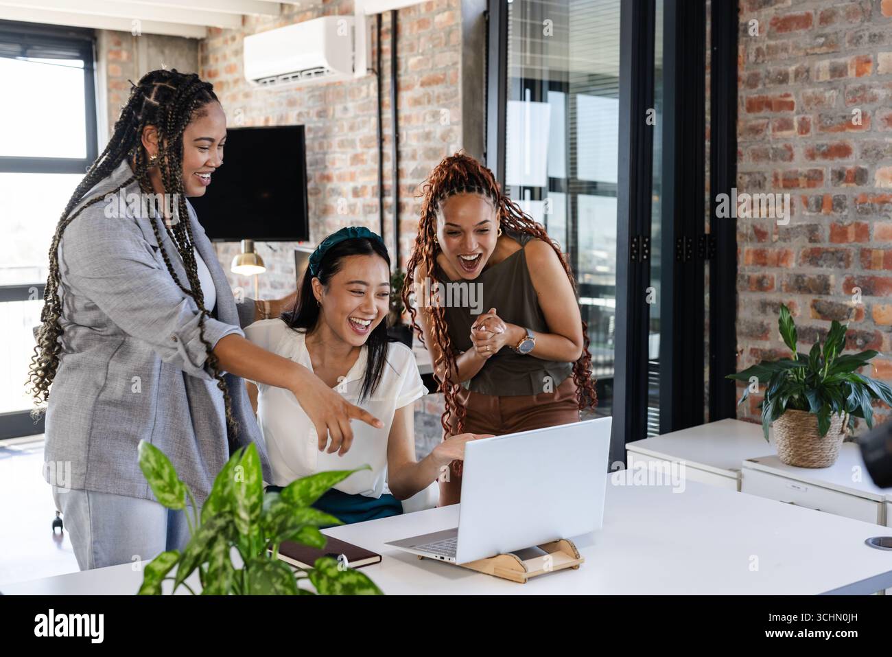 Enthousiastes collègues féminines diverses célébrant le succès tout en regardant un ordinateur portable dans un bureau moderne Banque D'Images