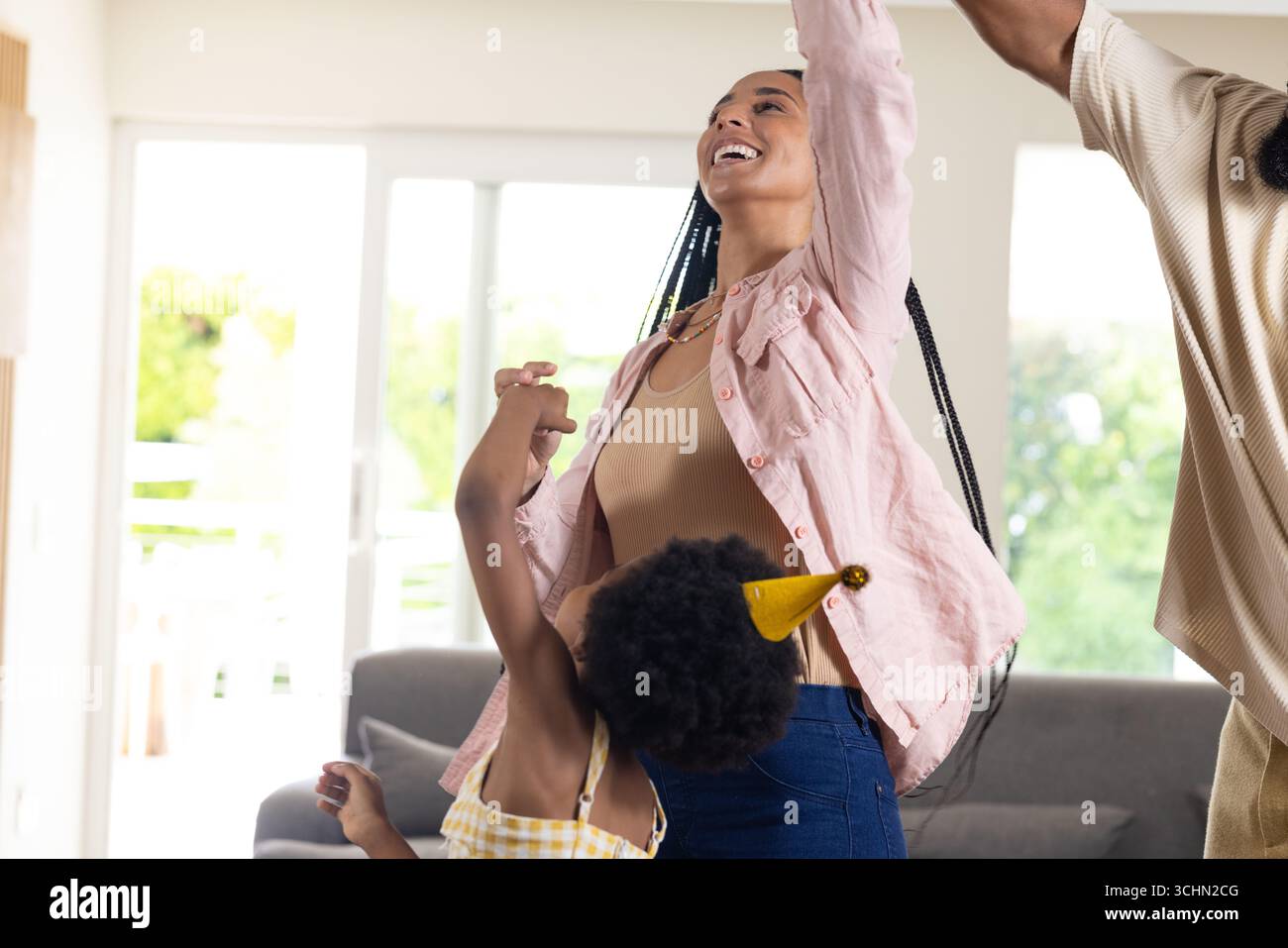 Famille célébrant à la maison, dansant joyeusement avec des chapeaux de fête et des sourires Banque D'Images