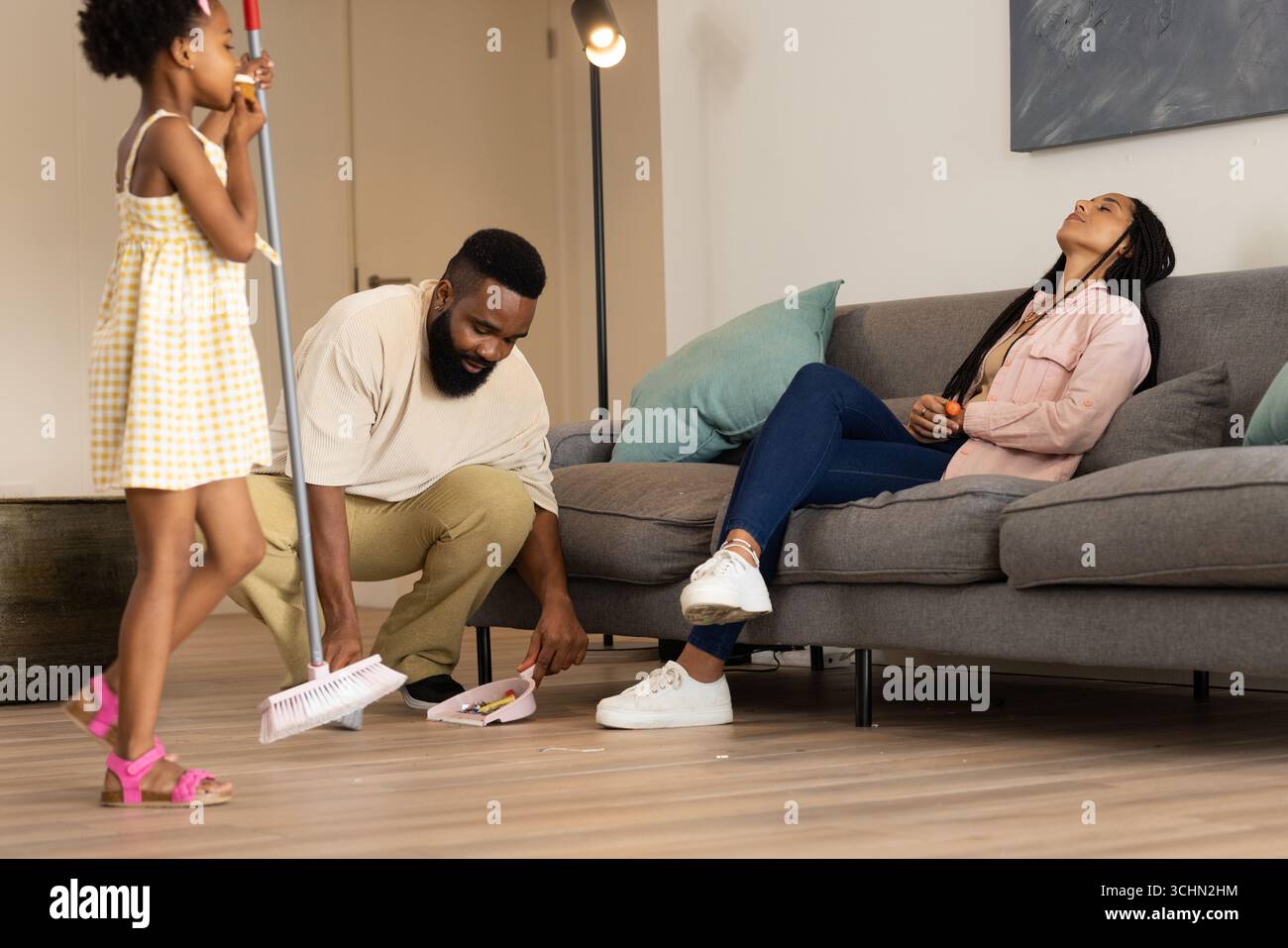 Famille afro-américaine nettoyant le salon, père balayant pendant que la fille aide Banque D'Images
