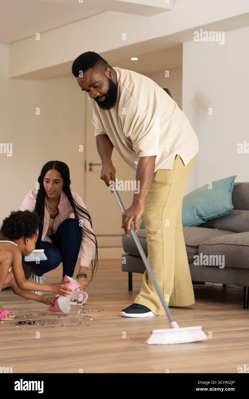 Famille nettoyant le salon ensemble, père balayant tandis que mère et enfant aident Banque D'Images