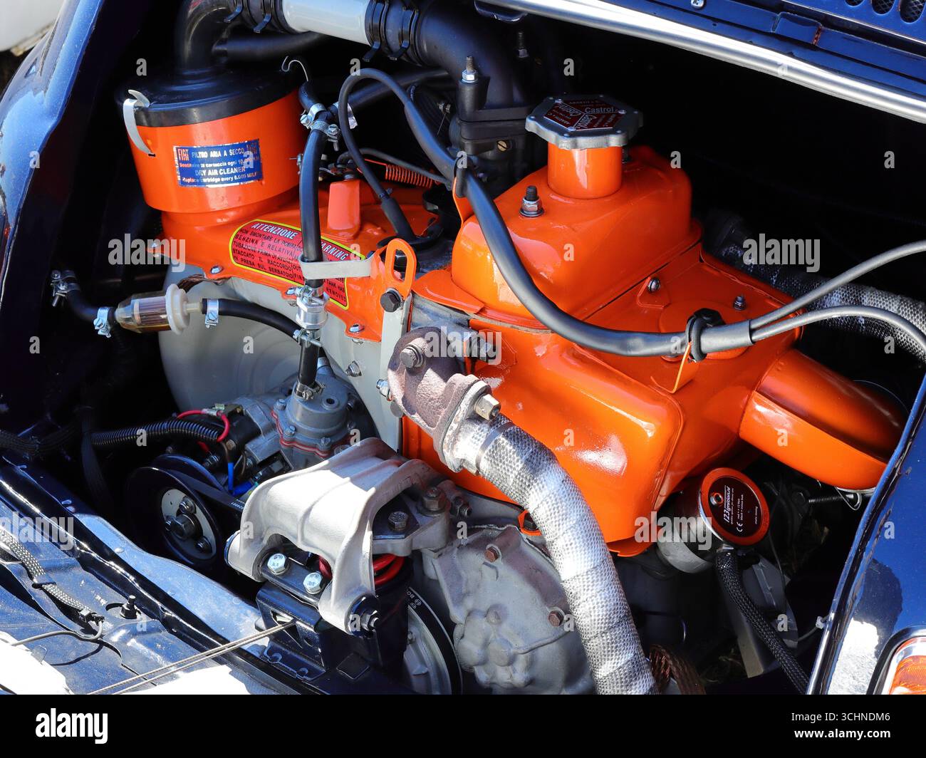 Un compartiment moteur de voiture classique est visible sur cette photographie, avec un bloc moteur et une culasse orange vif. Le moteur semble être une unité compacte, refroidie par air, probablement d'une Fiat 500 ou d'une petite voiture similaire. L'arrière-plan montre une partie de la carrosserie bleu foncé de la voiture. Illustration, éditorial : le rallye automobile de Stokes Bay à Gosport, Hampshire, Angleterre. 25 août 2025. Banque D'Images