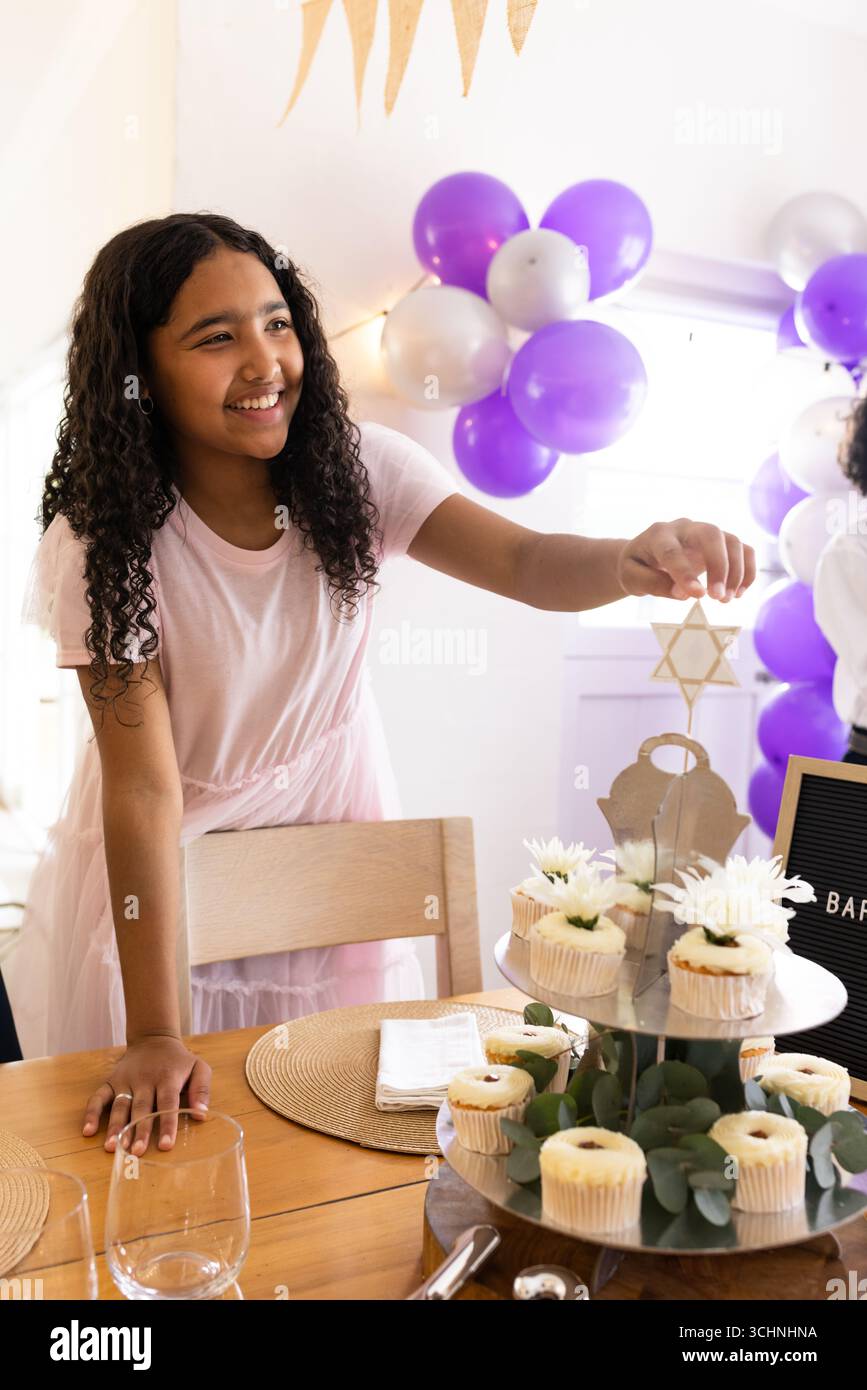 Fille souriante décorant des cupcakes avec Star of David lors de la célébration festive, à la maison Banque D'Images
