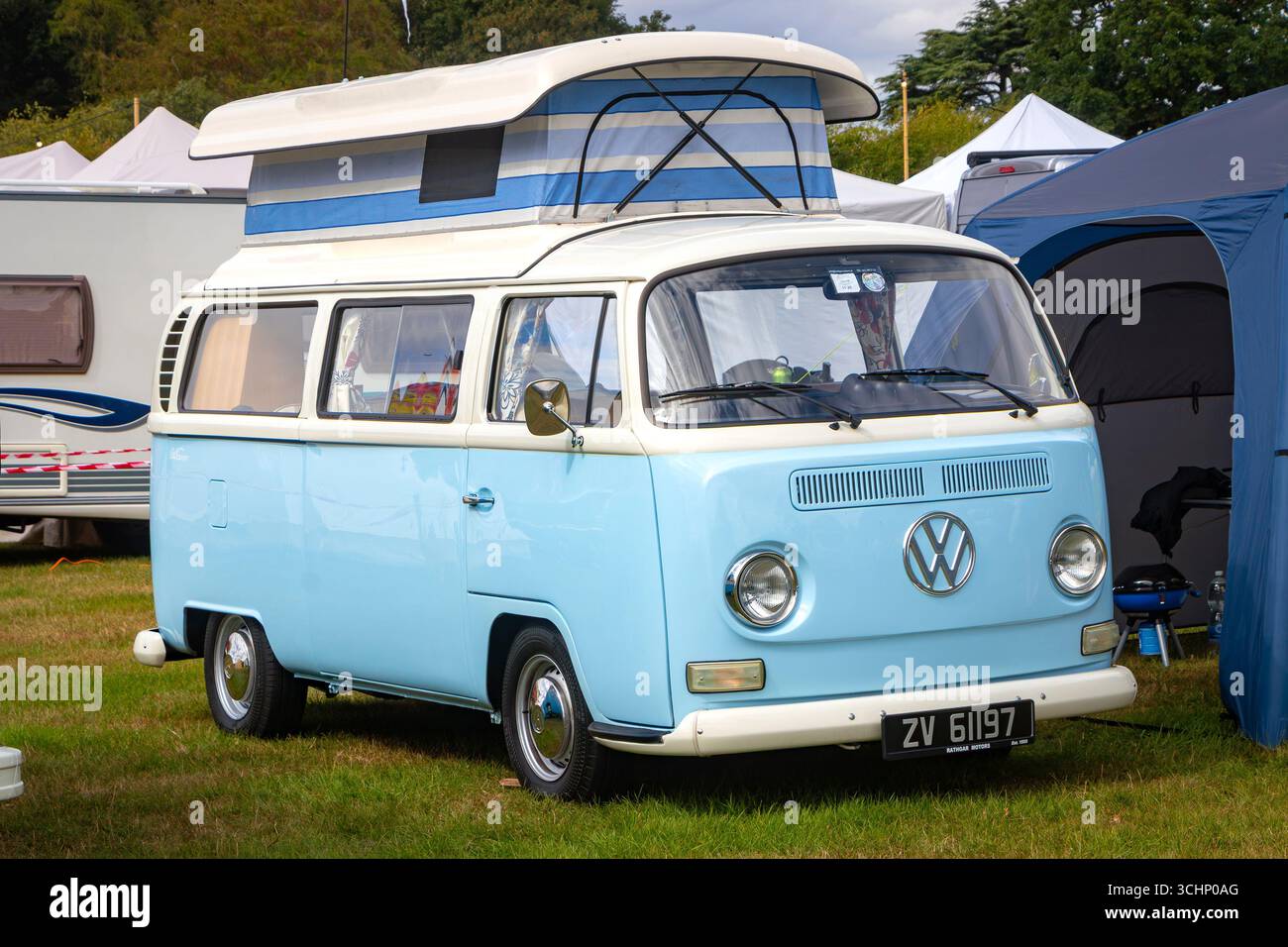 Camping-car Volkswagen bleu et blanc vintage avec toit escamotable dans un camping entouré de tentes et autres campeurs Banque D'Images
