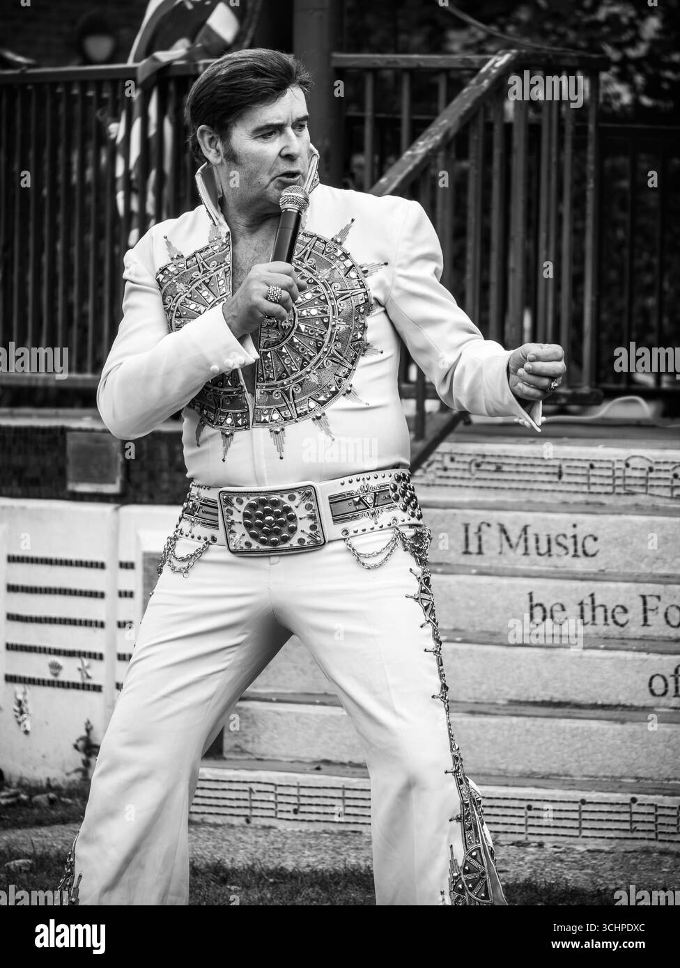 Un imitateur d'Elvis Presley se produisant au Oaklands Bandstand à Hythe, Kent, le 31 août 2025, capturé dans un ton noir et blanc Banque D'Images