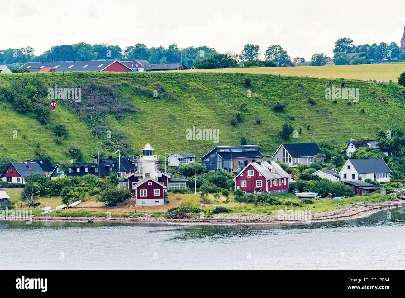 Phare de Hakens Fyr Île de Ven Oresund Suède // ÎLE DE Ven, Suède — le phare de Hakens fyr, ou phare de Haken, est une tour cylindrique blanche en béton située sur le promontoire est de l'île de Ven dans le détroit de Öresund. Construite à l'origine en 1890 comme une tour octogonale en bois, elle a été remplacée par la structure actuelle en 1939 et électrifiée en 1940. Le phare est remarquable pour être le premier au monde à employer un tyfon brumorne en 1923, une innovation significative dans l'histoire de la signalisation maritime. Hakens fyr reste une aide active à la navigation et est reconnu pour son rôle dans l’HE côtier suédois Banque D'Images