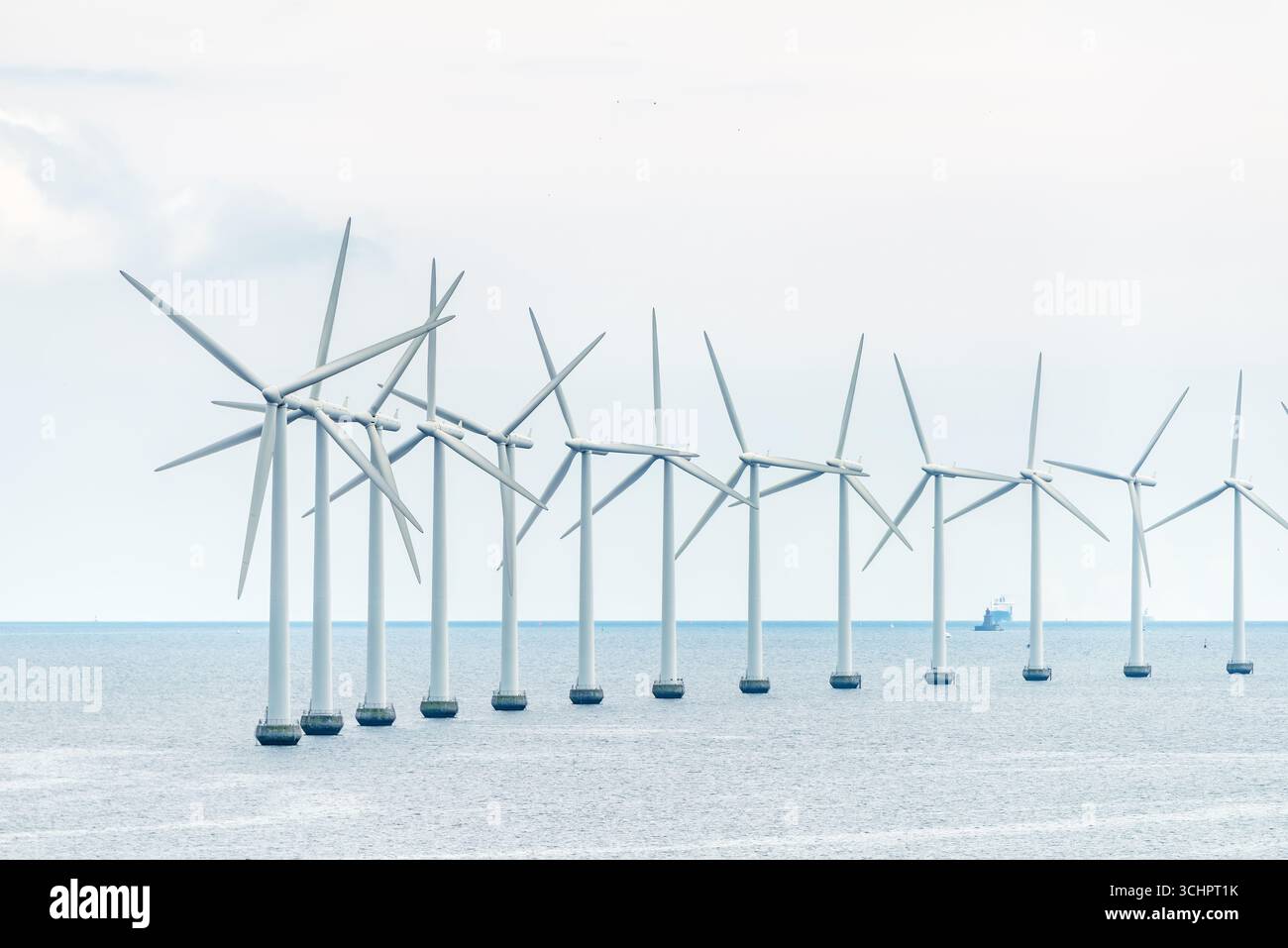 Ferry de Copenhague à Oslo // CHARLOTTENLUND, Danemark — Une rangée d'éoliennes offshore se dresse dans le détroit de Øresund, une voie navigable séparant le Danemark et la Suède. Les turbines font partie d’un parc éolien offshore, une source d’énergie renouvelable qui exploite l’énergie éolienne pour produire de l’électricité. Au loin, un cargo navigue dans les eaux, mettant en évidence l'importance du détroit comme voie de navigation. La scène capture l'intersection des infrastructures énergétiques modernes et de l'activité maritime dans la région de la capitale du Danemark. Banque D'Images