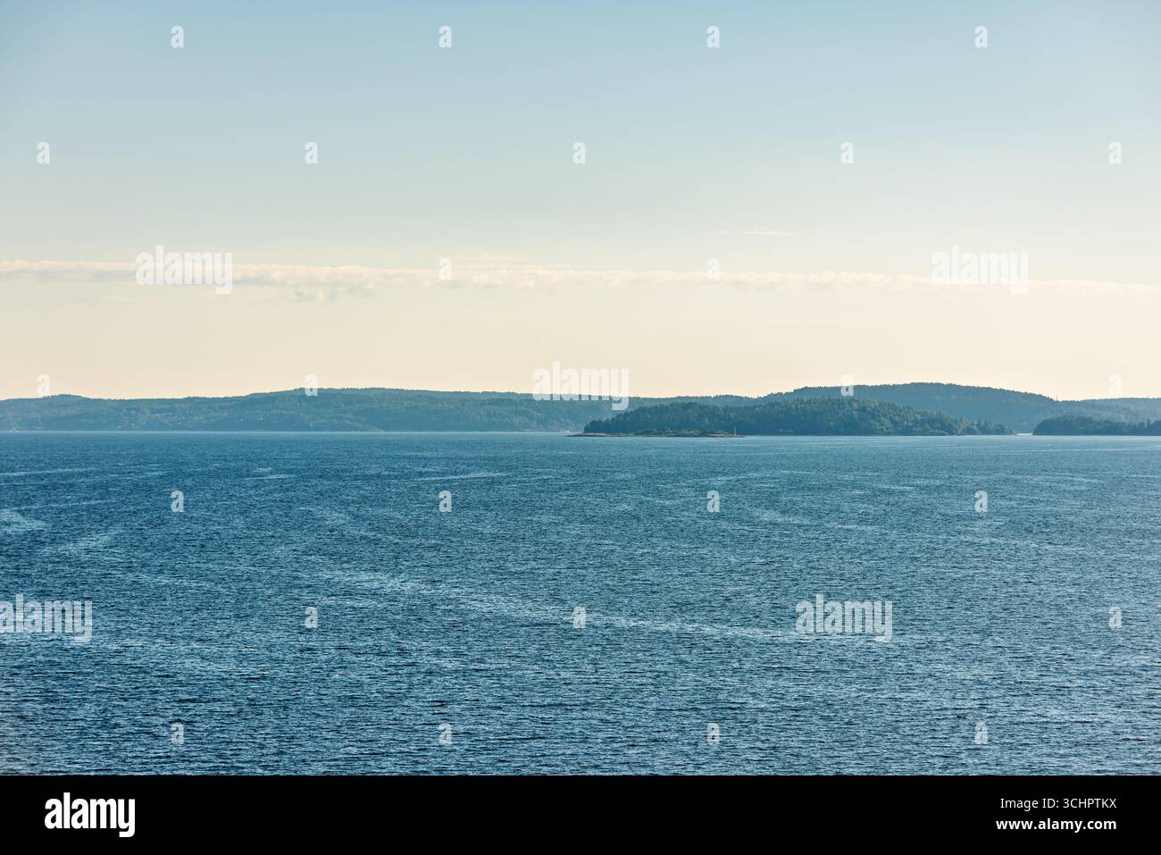 Oslofjord de Moss Norvège // Moss, Norvège — le Oslofjord, une entrée profonde de la mer de Norvège, est vu de la ville de Moss dans le comté de Østfold. Le fjord s'étend sur 107 kilomètres (66 miles) à l'intérieur des terres à partir du détroit de Skagerrak. Ses rives sont caractérisées par des collines ondulantes et des forêts denses, avec des colonies dispersées visibles le long du littoral. Le fjord d'Oslofjord est une voie navigable importante pour la Norvège, servant d'itinéraire majeur pour la navigation commerciale et la navigation de plaisance. Banque D'Images