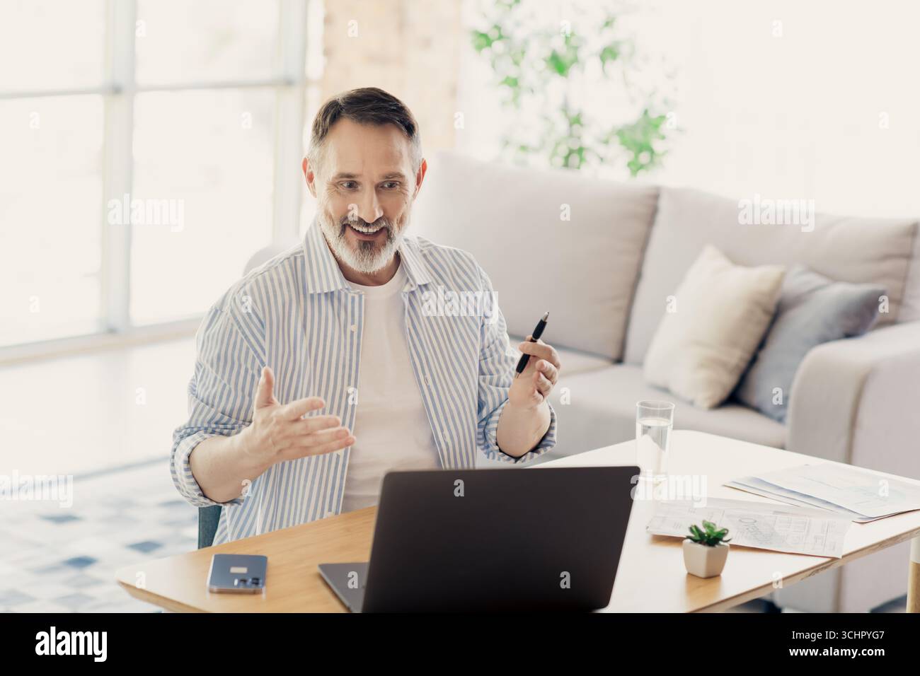 Homme d'affaires mature s'engageant dans une conférence en ligne de la maison avec un ordinateur portable, discutant des questions professionnelles en toute confiance Banque D'Images