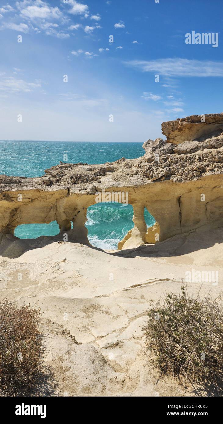 Une vue côtière à couper le souffle encadrée par une arche rocheuse, avec la mer qui s'écrase en dessous et un ciel lumineux en arrière-plan. Banque D'Images